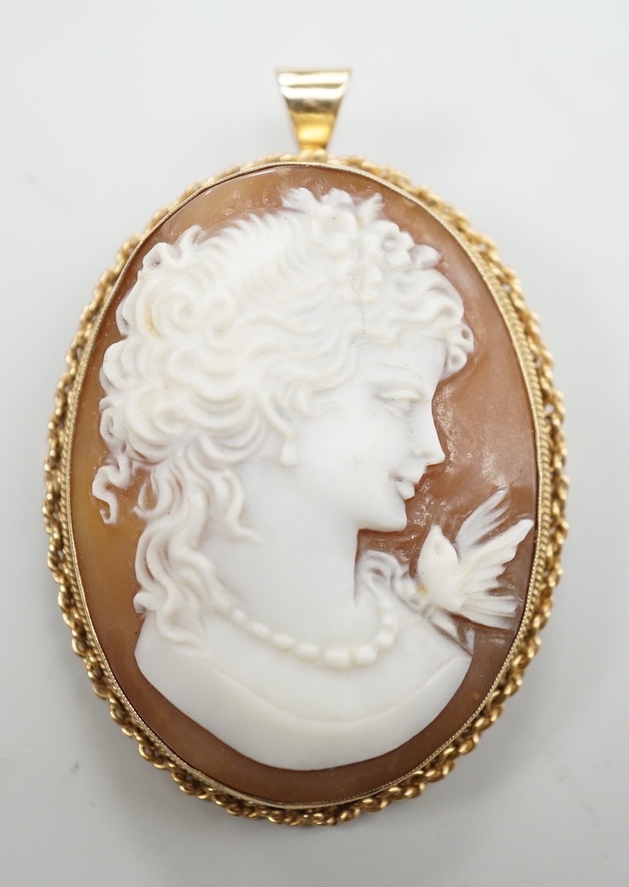 A modern 9ct gold mounted oval cameo shell pendant brooch, carved with a bird and bust of a lady to sinister, overall 49mm